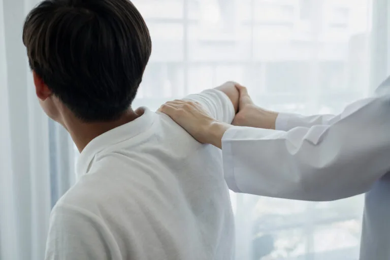 Female physiotherapists provide physical assistance to male patients with shoulder injuries massage their shoulders for muscle recovery in the rehabilitation center. Physiotherapy concepts.