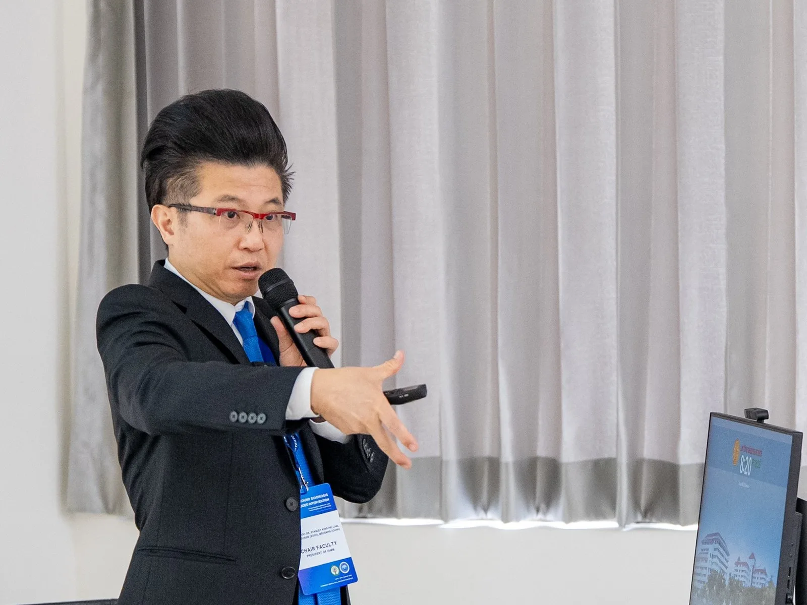Stanley Lam 醫師在課堂上手持麥克風講解，身後為投影螢幕。