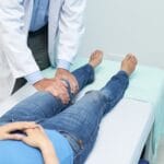 醫師在診療床旁用雙手檢查患者的膝關節