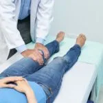 醫師在診療床旁用雙手檢查患者的膝關節