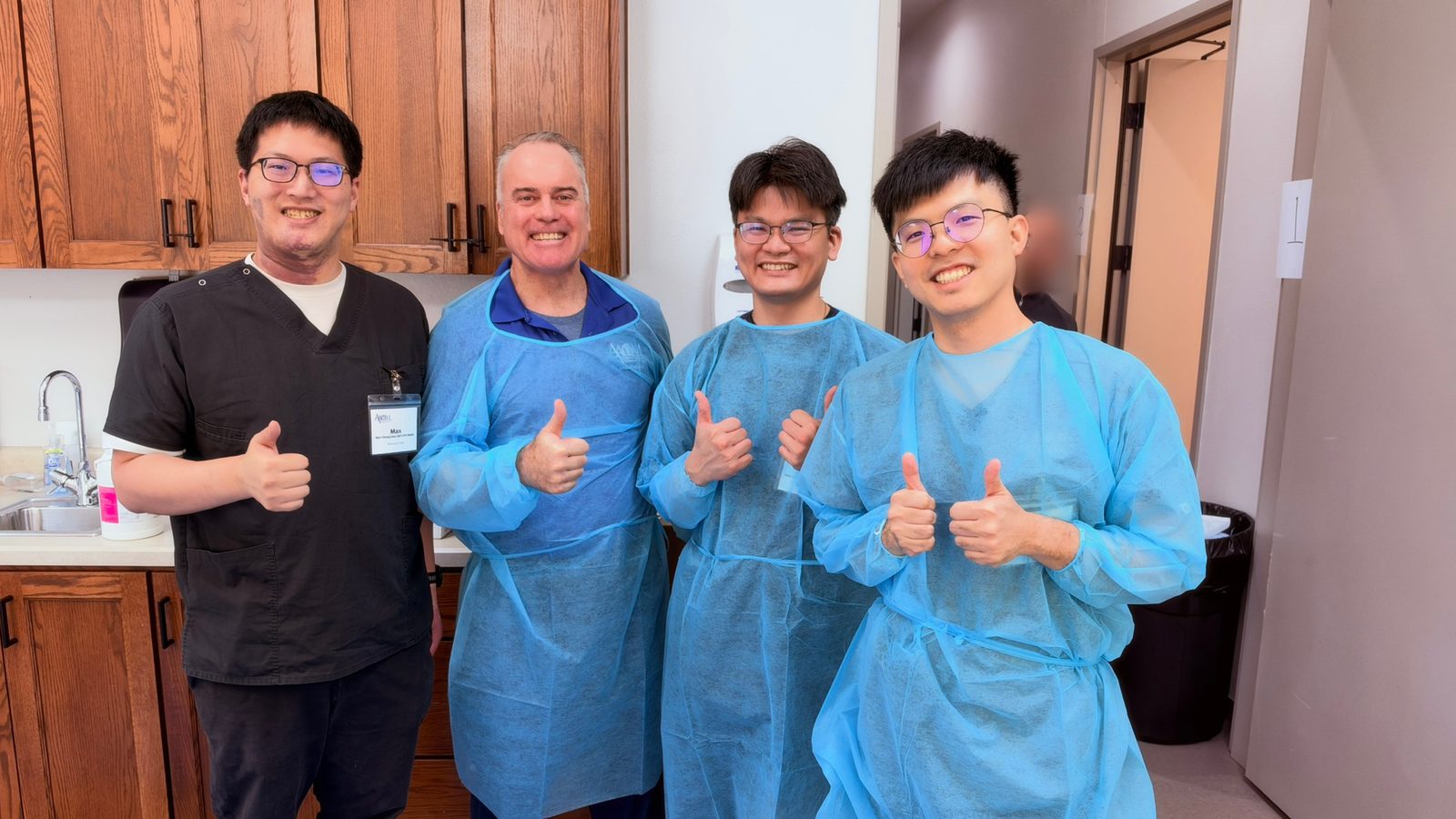 四位醫師在工作坊教室比讚合照，一位穿黑色刷手服、三位穿藍色隔離衣