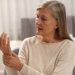 腕隧道症候群：臥室裡坐在椅子上的中年女性，一手握住另一側手腕，看著舉起的手