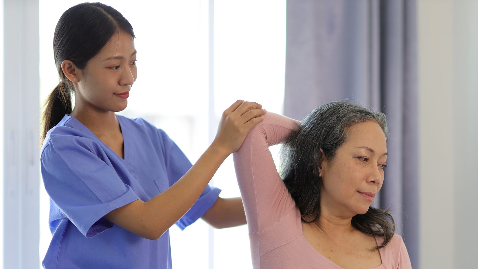 治療師扶著中年女性的手肘,協助她把手臂舉過頭