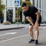 髂脛束症候群：跑者停在市區路邊，彎腰用雙手按著膝蓋