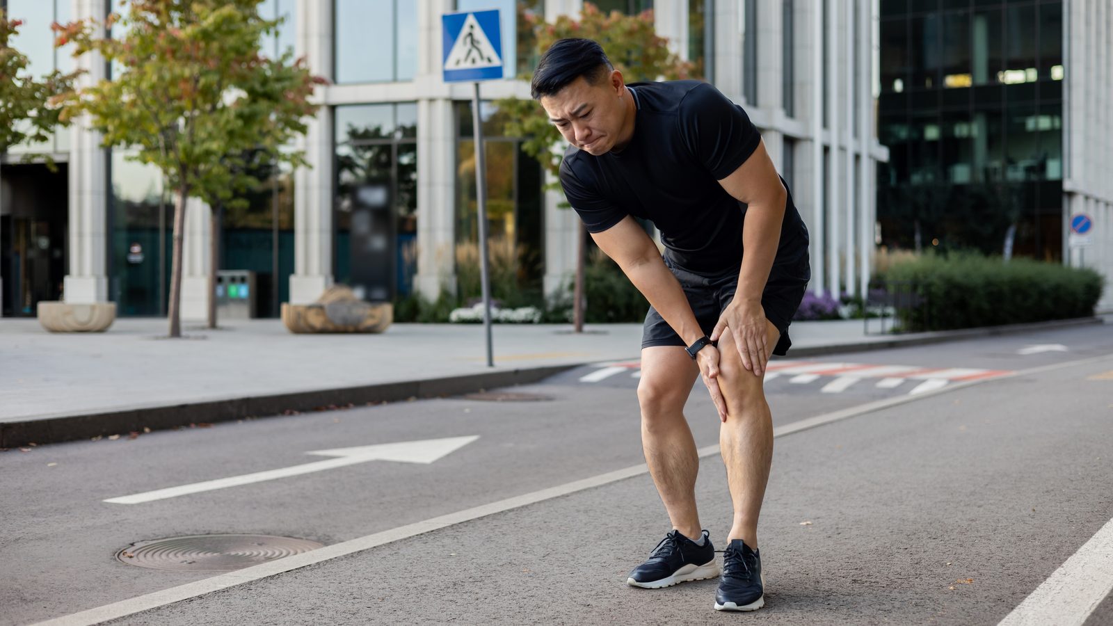 髂脛束症候群:跑者停在市區路邊,彎腰用雙手按著膝蓋